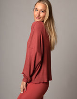 woman wearing oversized waffle knit long sleeve top in papaya red orange on grey background