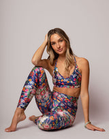 Woman wearing a colorful floral outfit sitting on the floor against a plain background