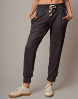 Person wearing dark gray jogger pants with a plain background