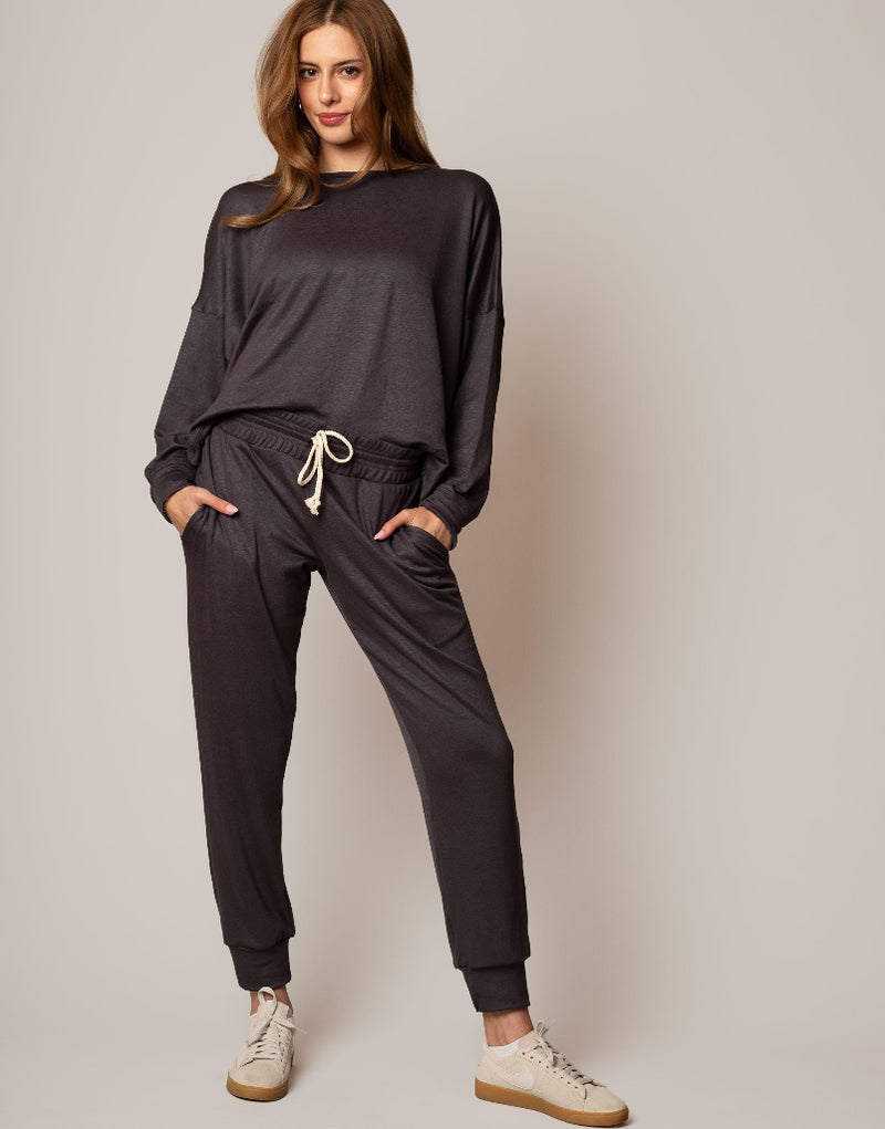 Woman wearing a dark gray tracksuit with beige shoes on a light gray background