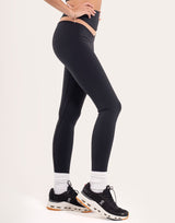 A model wearing high-waisted black athletic leggings, white crew socks, and black running shoes with white and orange soles, shown from the waist down against a plain off-white studio background.