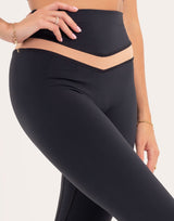 Close-up of a model wearing high-waisted black leggings with a beige V-shaped waistband detail, set against a plain light background.