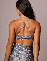 Rear view of a woman wearing a floral print sports bra and matching high-waisted bottoms against a solid taupe background.