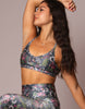 A woman modeling a matching floral print activewear set, featuring a sports bra and high-waisted leggings, posed against a solid neutral background.
