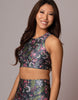A woman modeling a matching two-piece activewear set featuring a dark gray floral print with pink, green, and white botanical details, set against a solid gray studio background.