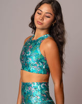 A woman modeling a matching two-piece athletic set featuring a vibrant teal green color with a pink and white floral pattern, set against a solid gray studio background.