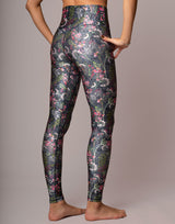 A person wearing high-waisted leggings with a dark gray and black base and an all-over floral print in pink, white, and green, shown from the back against a plain studio background.