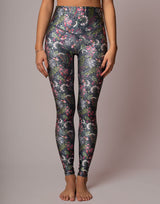 A model is shown from the waist down wearing high-waisted leggings with a dark gray base and a dense, colorful floral and bird pattern in pink, green, white, and blue.