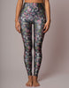 A model is shown from the waist down wearing high-waisted leggings with a dark gray base and a dense, colorful floral and bird pattern in pink, green, white, and blue.
