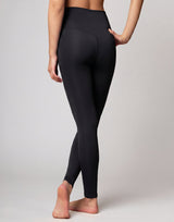 A model from the back wearing black high-waisted leggings, standing barefoot against a light gray studio background.