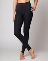 A model wearing black high-waisted maternity leggings, shown from the waist down against a neutral light gray studio background.