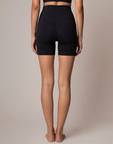 Rear view of a model wearing black high-waisted athletic shorts against a solid beige studio background.