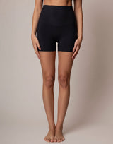 A model from the waist down wearing high-waisted black athletic shorts against a neutral beige studio background.