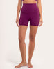 A model wearing high-waisted, form-fitting athletic shorts in a deep magenta-purple color, shown from the waist down against a plain off-white studio background.