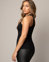 Woman wearing a black tank top and black leggings against a neutral background