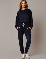 Woman wearing a navy blue tracksuit with white sneakers on a beige background