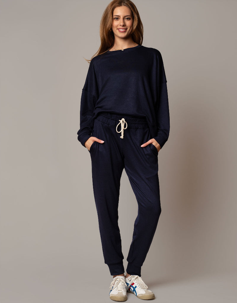 Woman wearing a navy blue tracksuit with white sneakers on a beige background