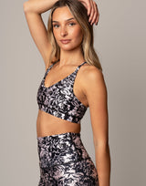 Woman wearing a black and white floral sports bra and leggings on a gray background