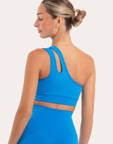 A woman shown from the back wearing a bright blue athletic sports bra and matching high-waisted leggings against a light gray studio background.