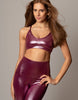 Woman wearing a shiny maroon sports bra and leggings against a neutral background