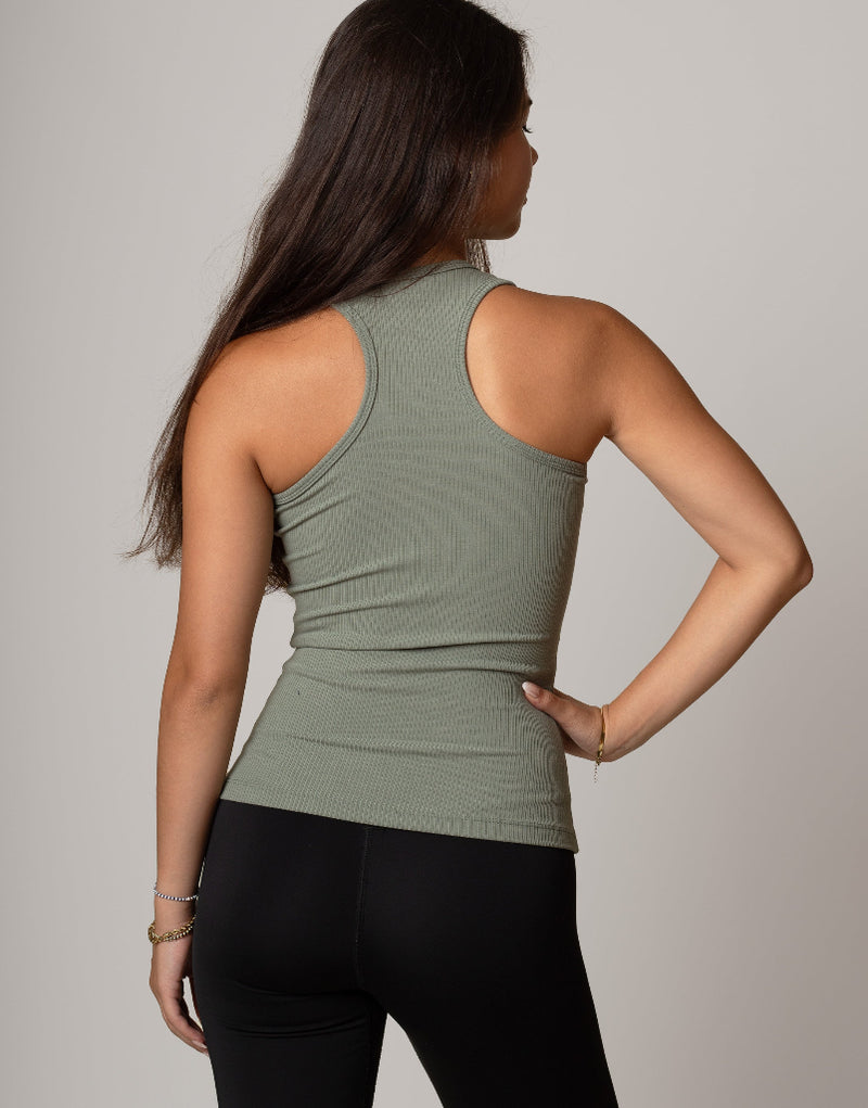 Woman wearing a green tank top and black leggings against a plain background