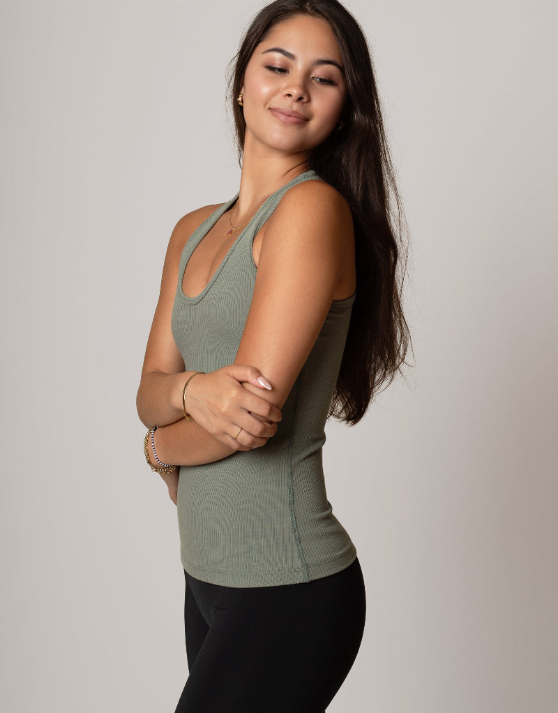 Woman wearing a green tank top and black leggings against a plain background