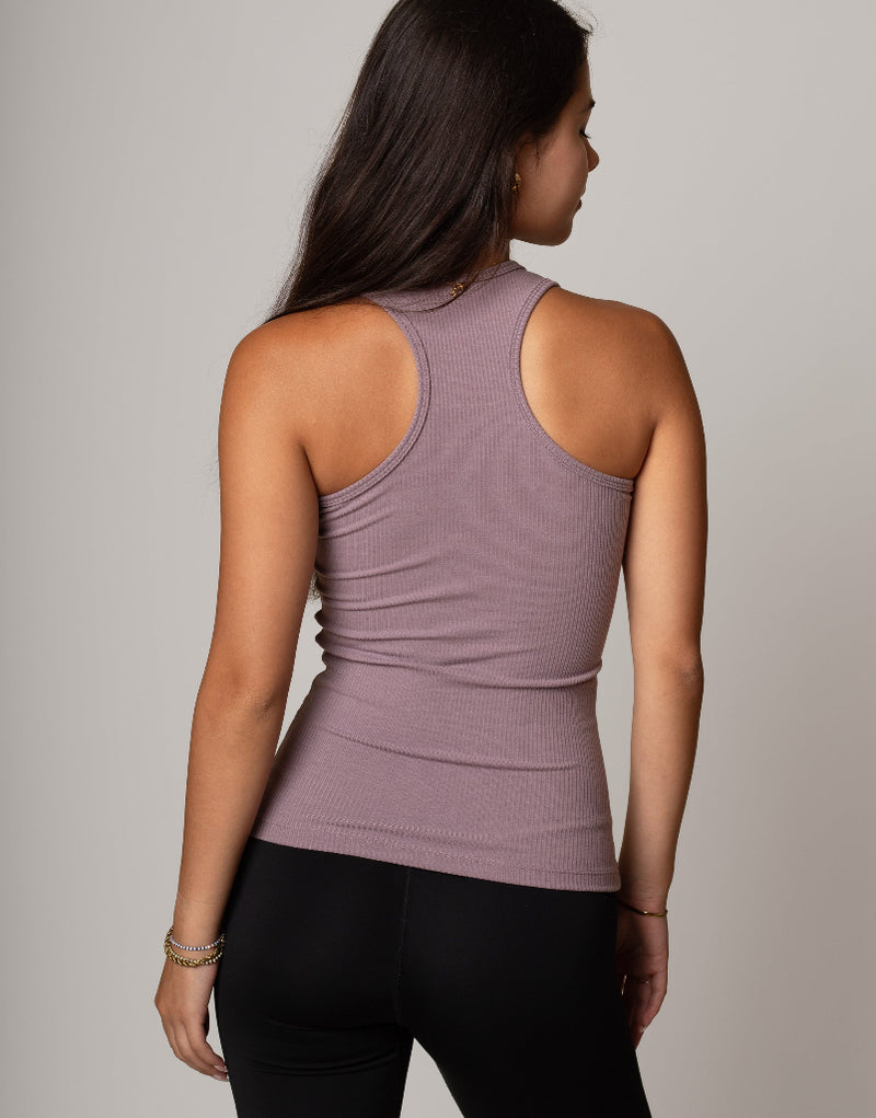 Woman wearing a mauve tank top and black leggings against a gray background
