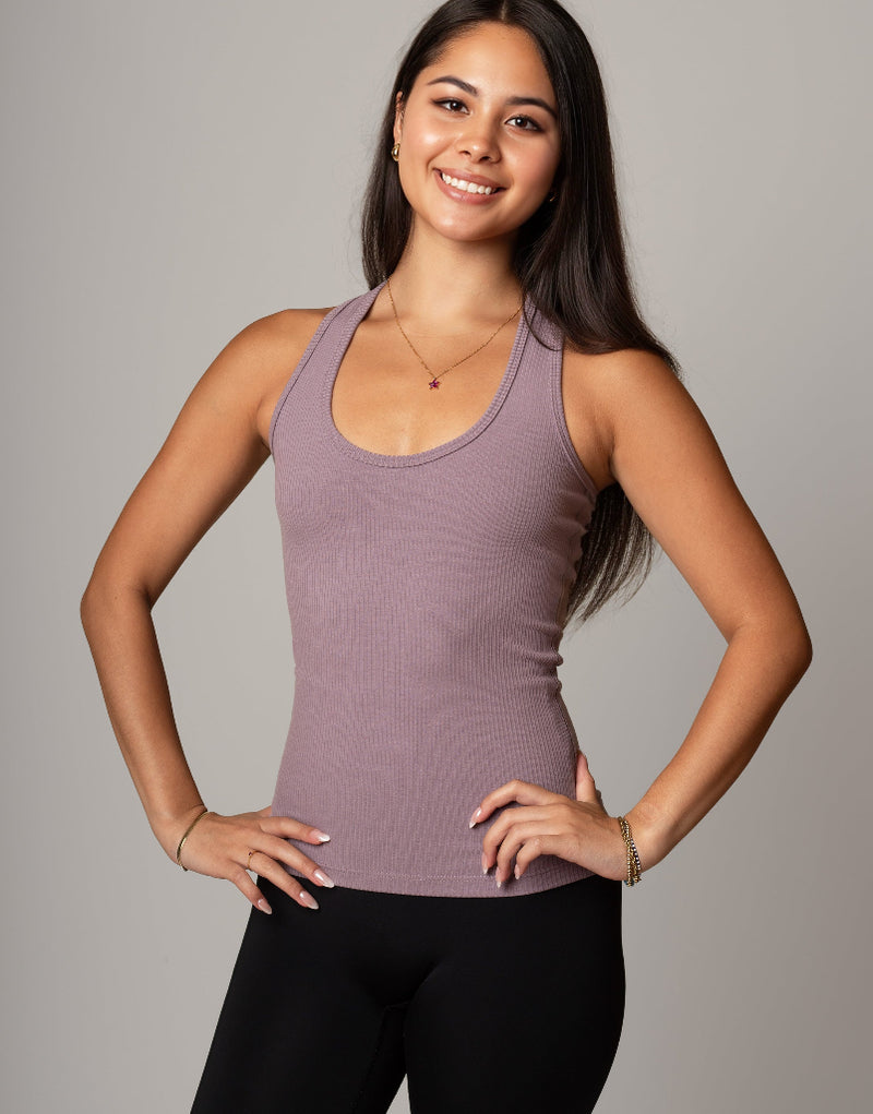 Woman wearing a mauve tank top and black leggings against a gray background