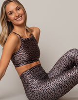 Woman wearing a leopard print sports bra and leggings on a plain background