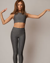 Woman wearing gray athletic top and leggings against a plain background