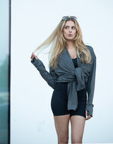 Woman wearing a gray jacket over a black top and shorts against a light background