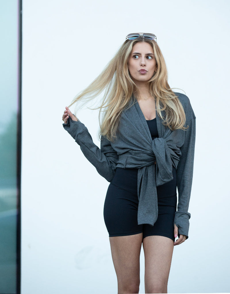 Woman wearing a gray jacket over a black top and shorts against a light background