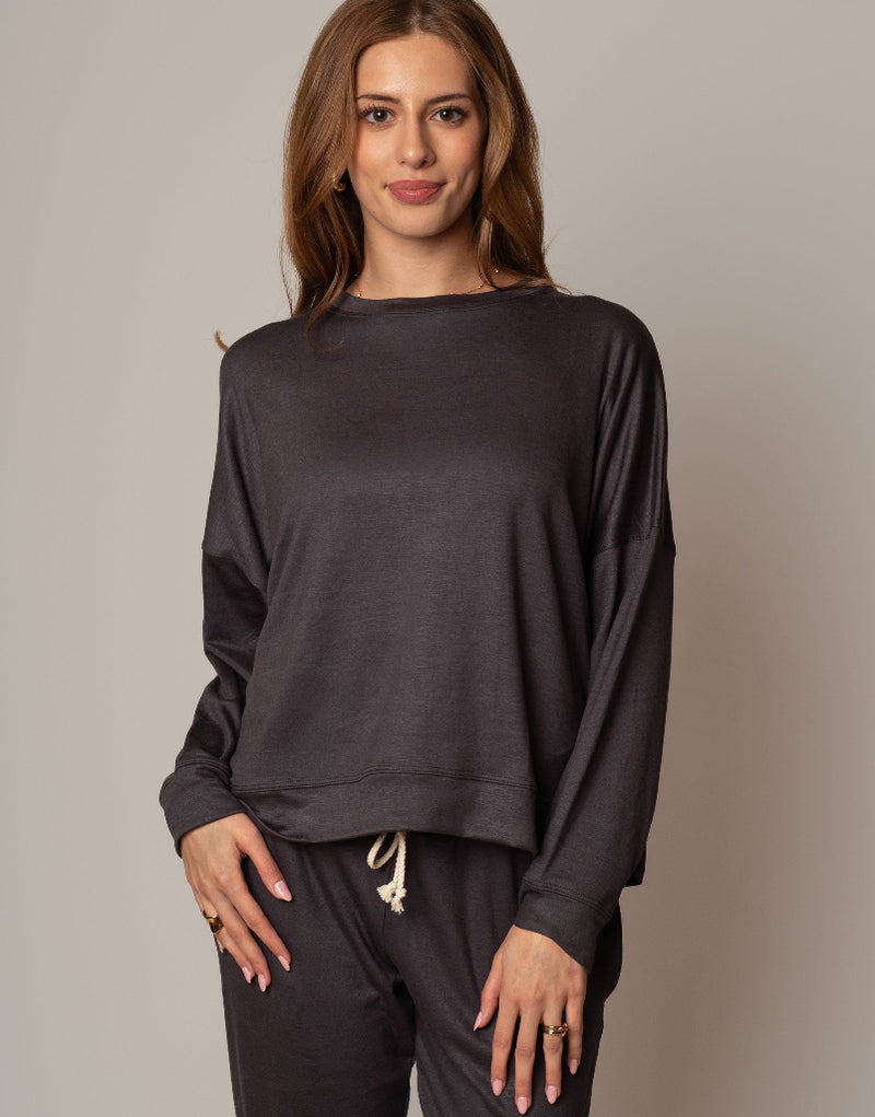 Woman wearing a dark gray long-sleeve top and pants against a plain background