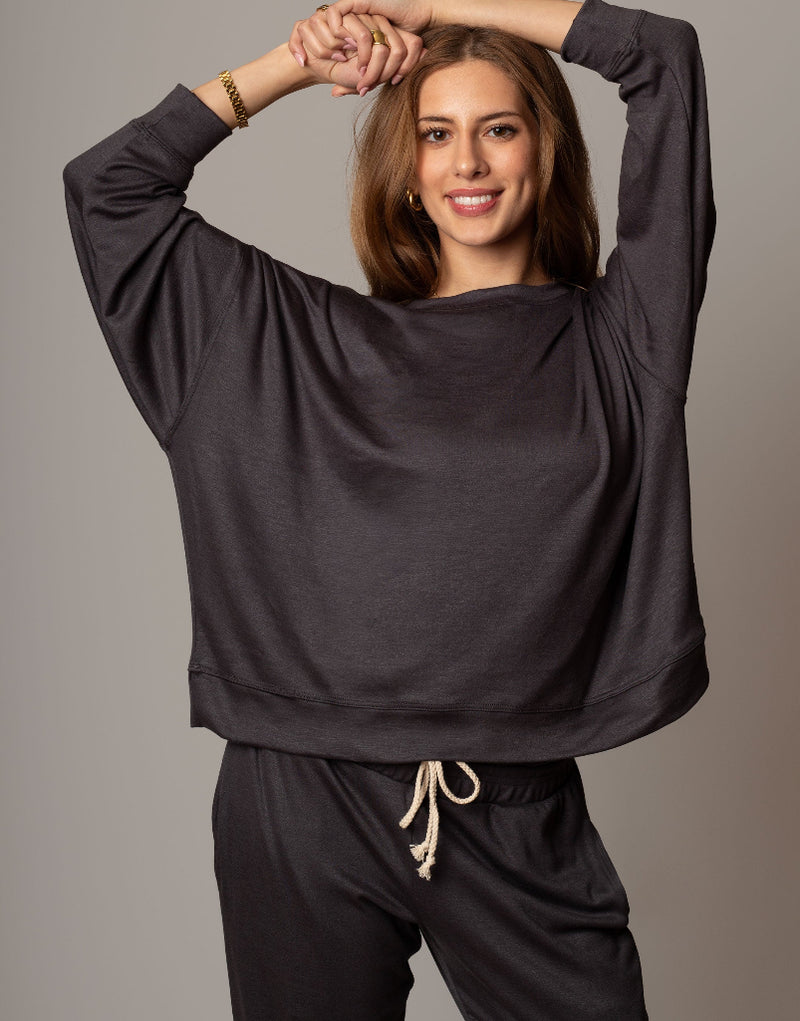 Woman wearing a dark gray oversized top and pants on a plain background