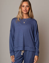 Woman wearing a blue sweatshirt and pants against a gray background